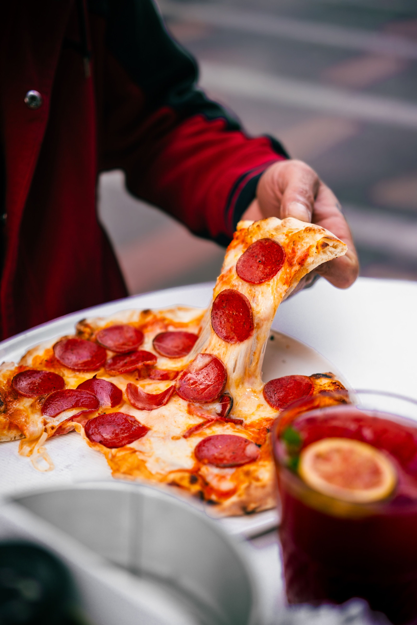 A hand pulling a slice of pepperoni pizza from the tray